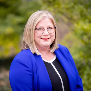 Erin Shetler smiles for a photo in front of some greenery outside.